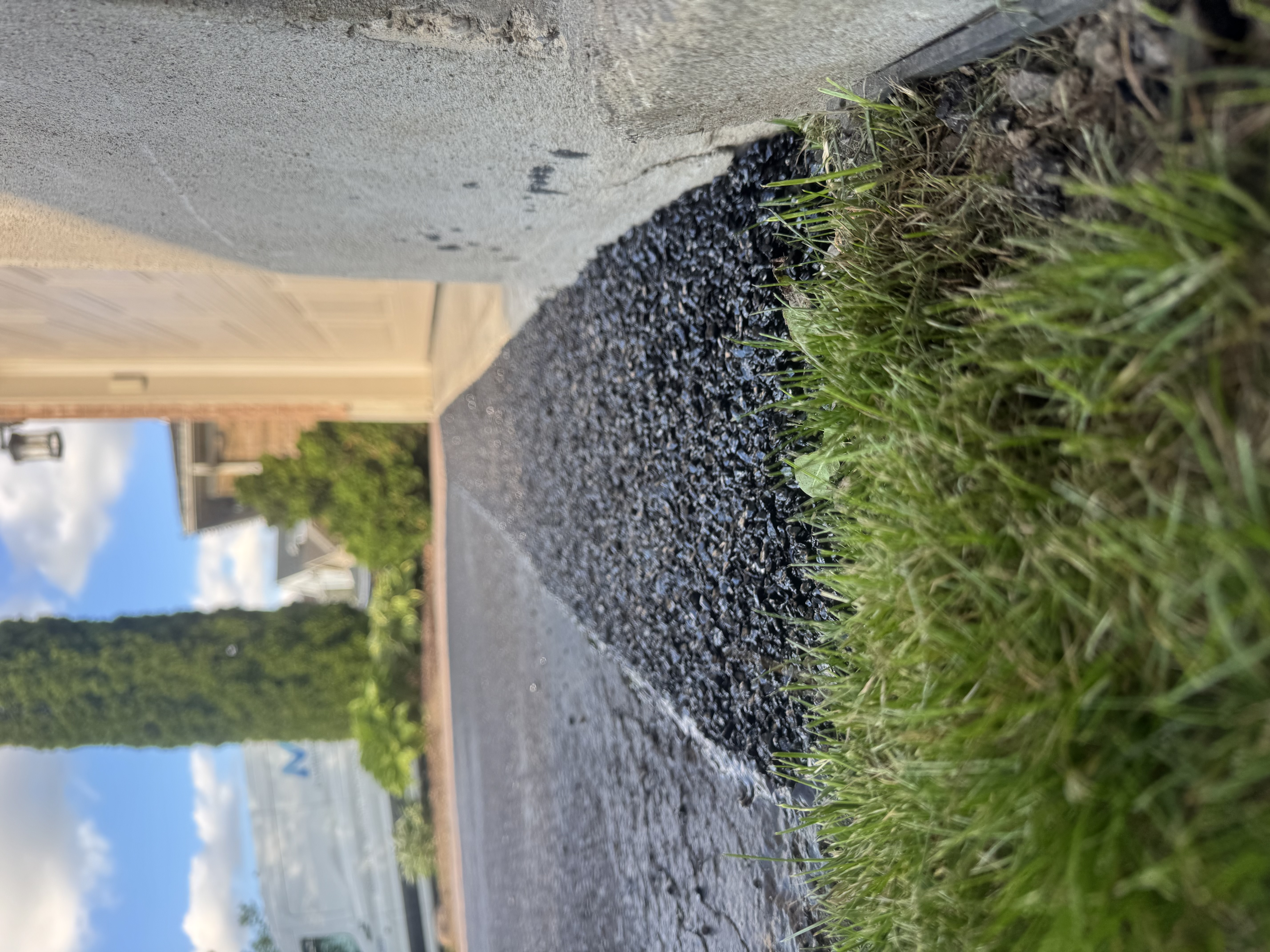 Side view of cold patch asphalt garage ramp showing smooth taper between concrete lip and driveway