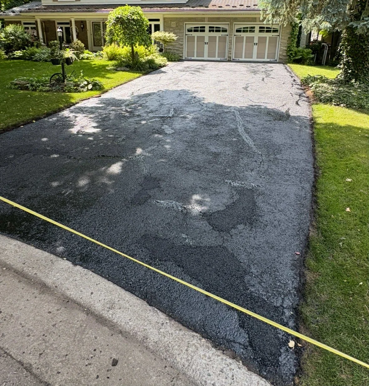 Newly paved driveway in front of a house with a garage, bordered by green grass and landscaping.