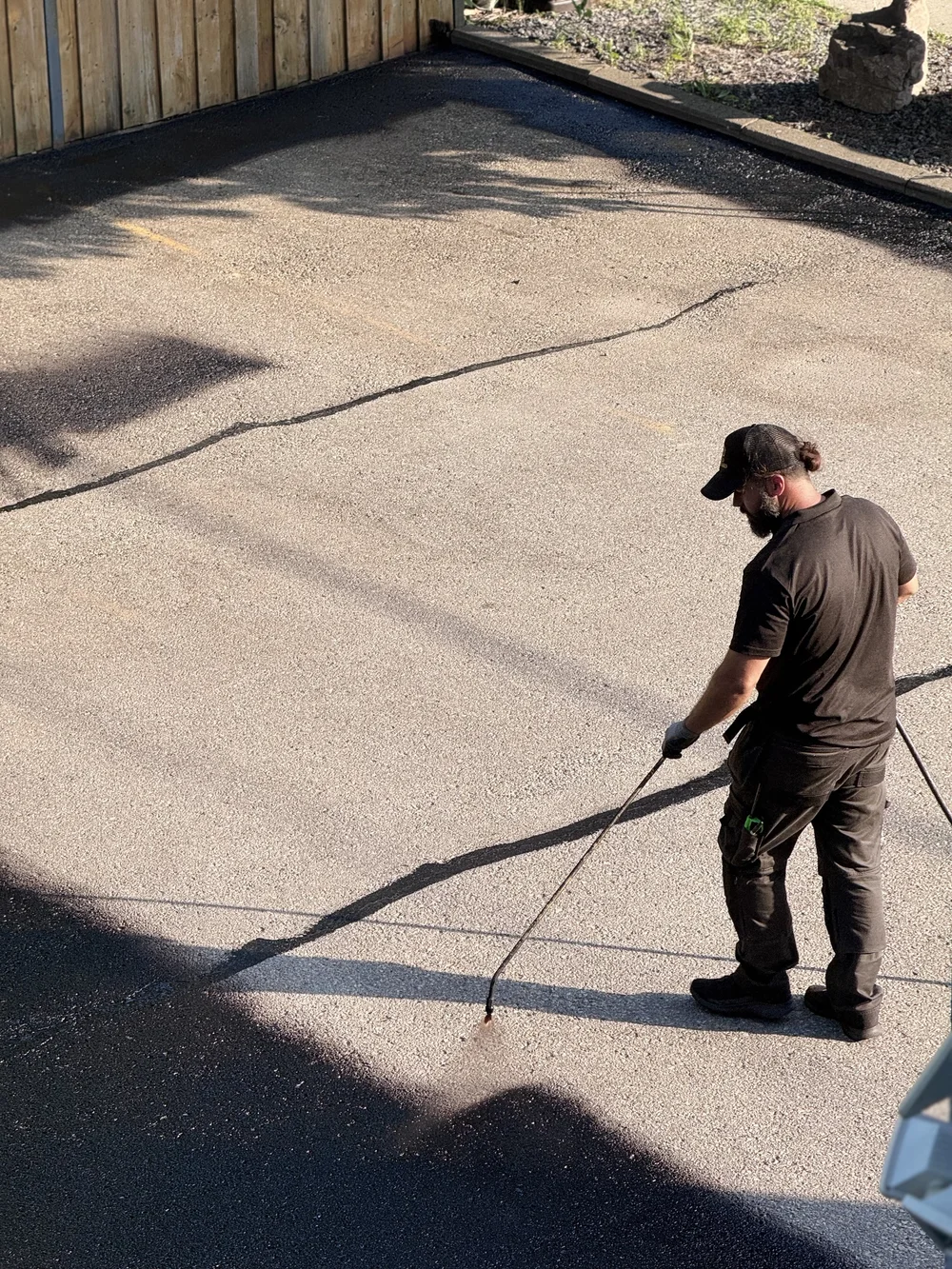 An image of a worker for Gold Standard Property Pros sealing an asphalt parking lot after completing asphalt pothole repairs and rubberized asphalt crack filling services