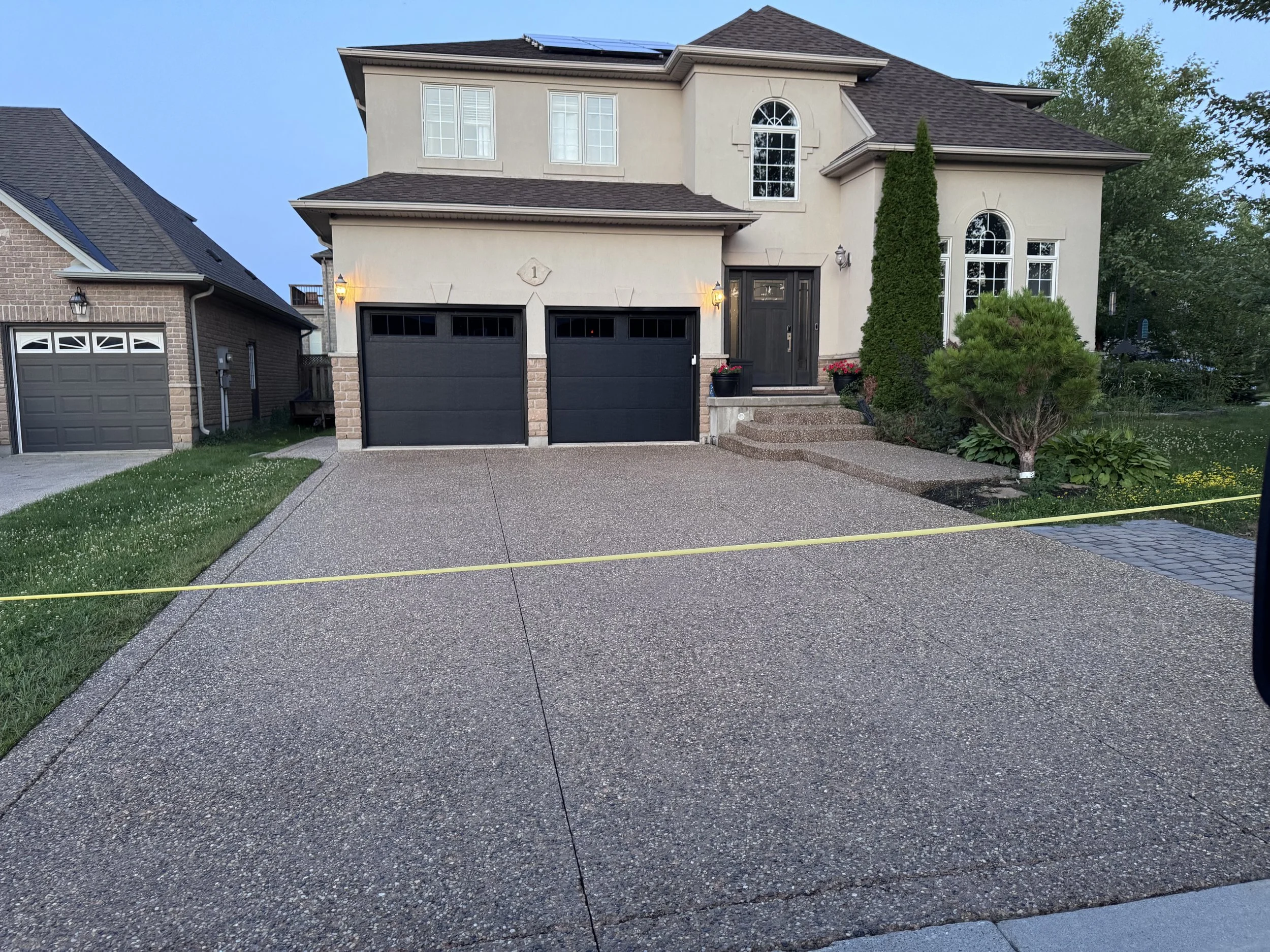 Front view of a two-story house with a double garage, a dark door, and landscaping, with a small lawn and bushes.