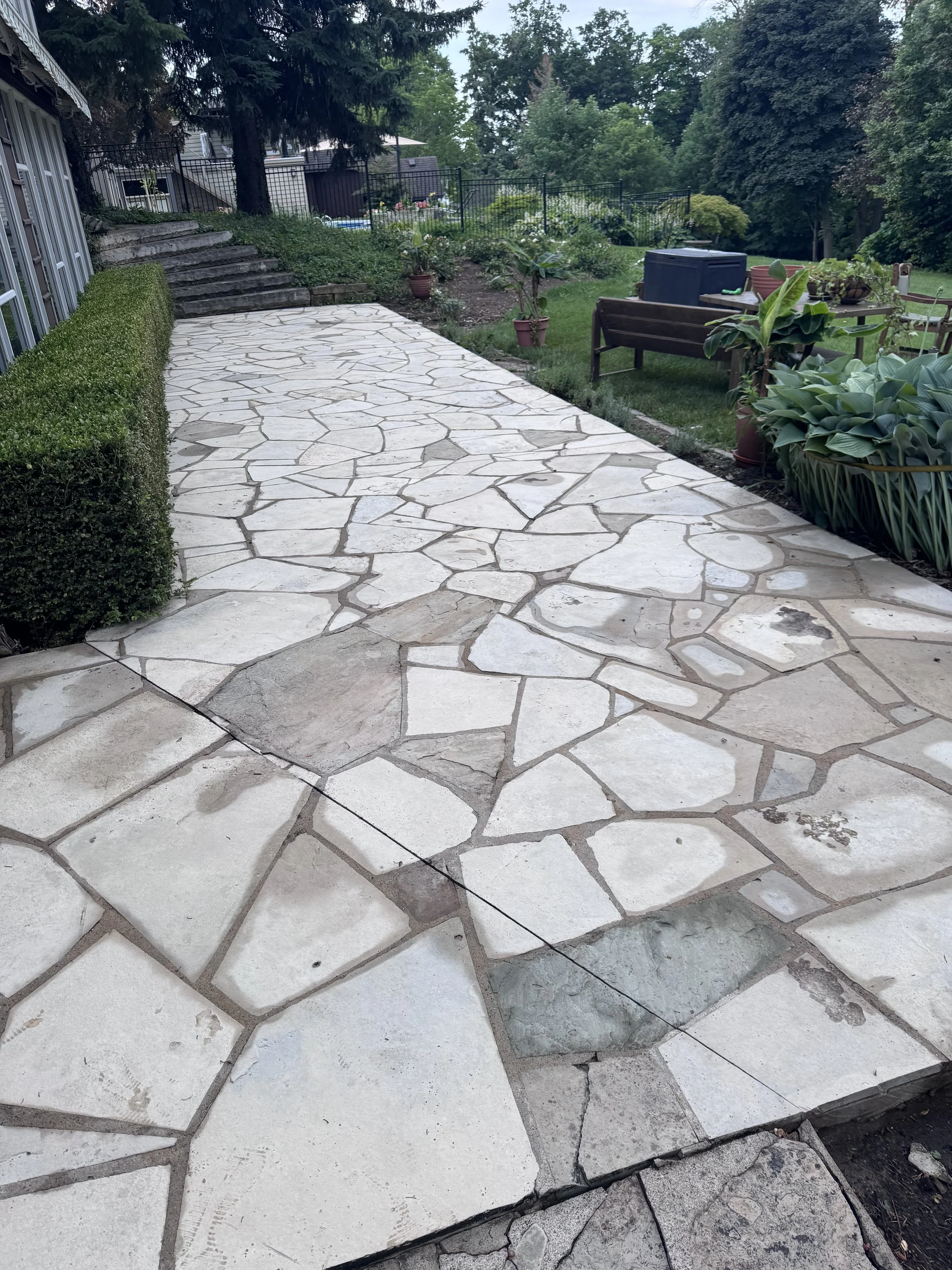 A stone sidewalk in a backyard with a garden and trees around.