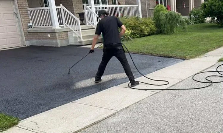 Technician pressure washing an asphalt driveway in Kitchener-Waterloo to prepare it for asphalt driveway sealing
