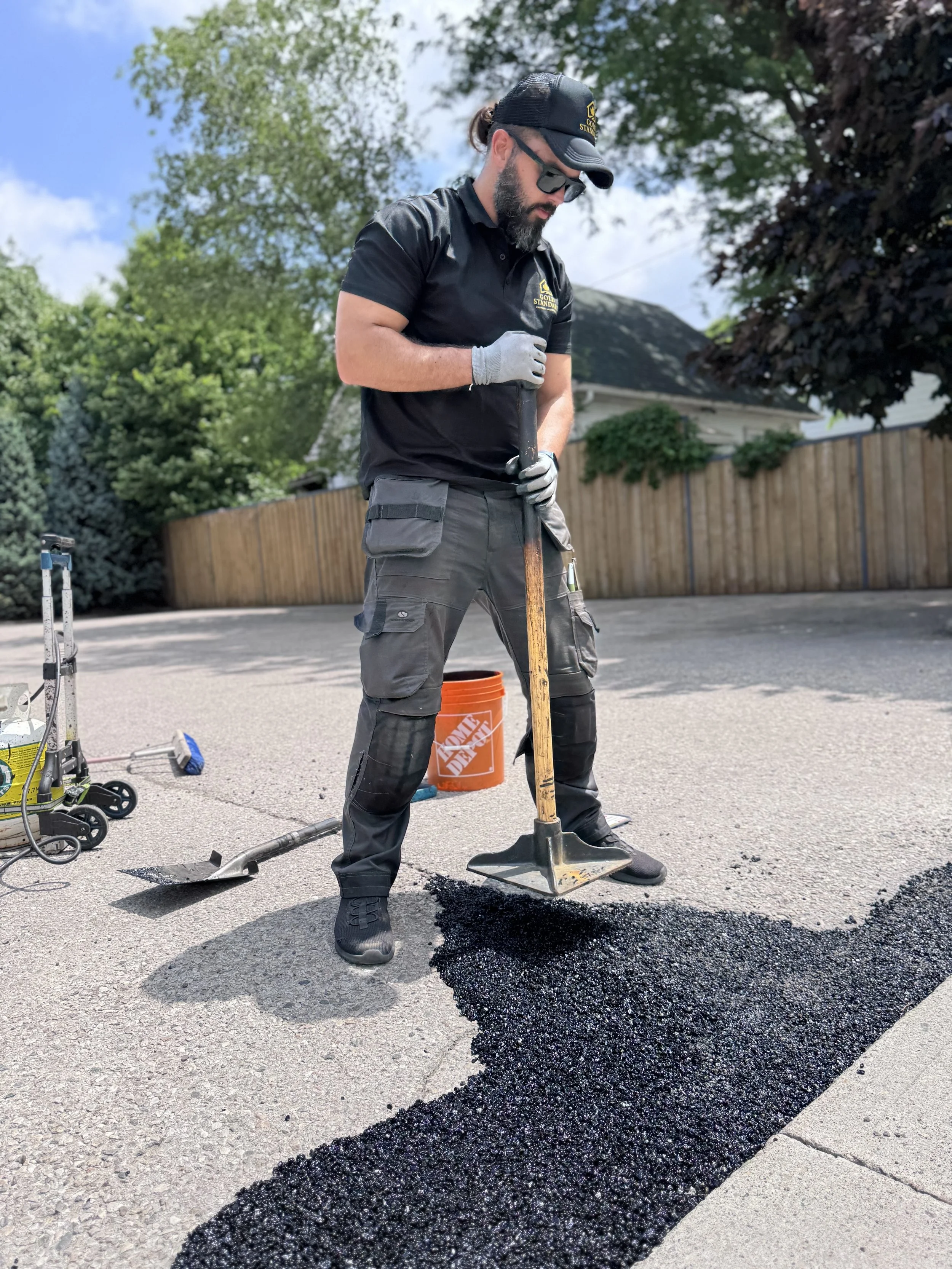 As image of asphalt pothole repair and a worker tamping down fresh asphalt with a tool