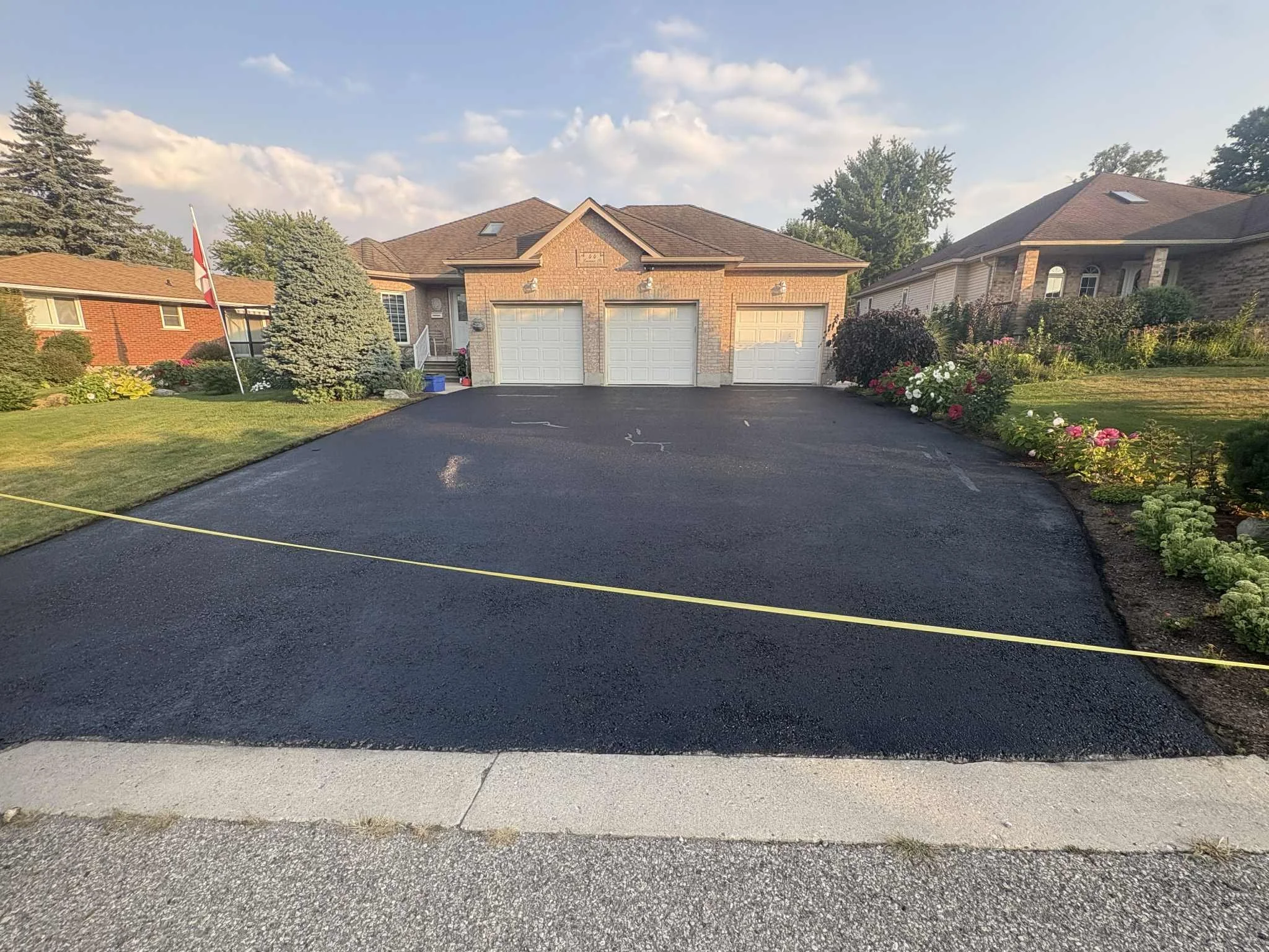 Finished matte black asphalt driveway after asphalt driveway sealing, with a measuring tape stretched across the surface