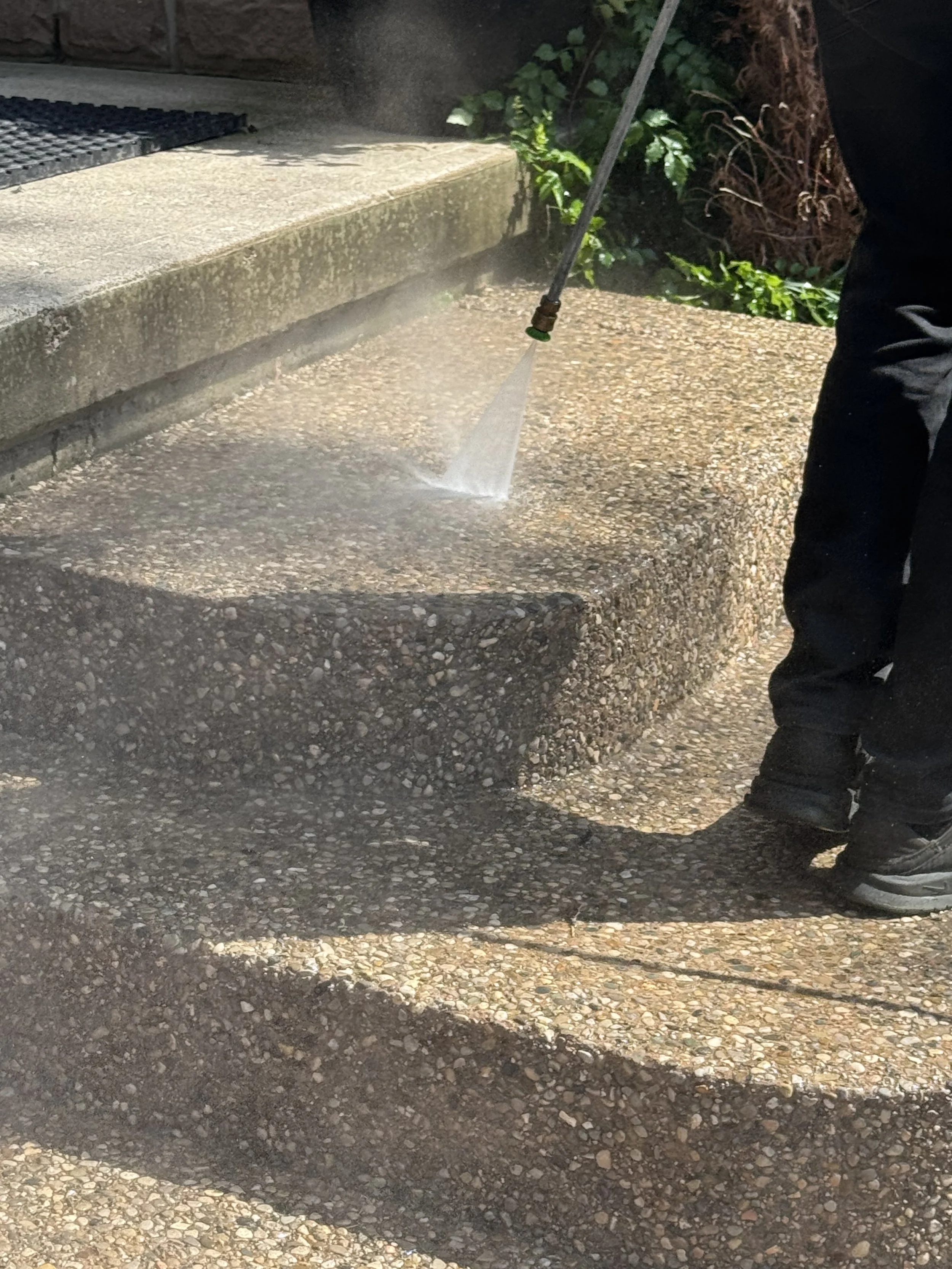 Person pressure washing concrete stairs outside.